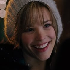 a smiling woman wearing a knitted hat and fur coat with lights in the background