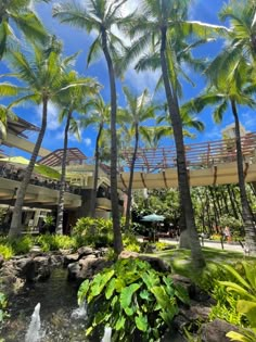 palm trees are in the foreground, and people walk on the other side of the building