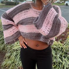 a woman standing in front of some bushes wearing a pink and grey crochet sweater