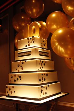 a large white cake sitting on top of a table with gold balloons around it and the number forty