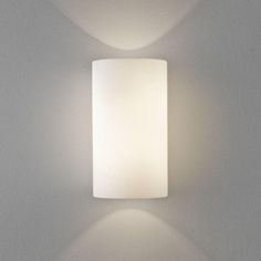 a white wall light mounted on the side of a wall next to a lamp shade