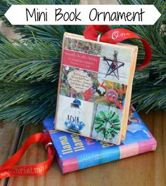 mini book ornament sitting on top of books next to a christmas tree with red ribbon