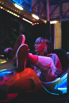 a woman is sitting in a bumper to bumper ride at night with her feet on the ground