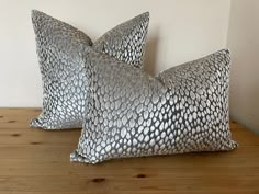 two silver pillows sitting on top of a wooden table