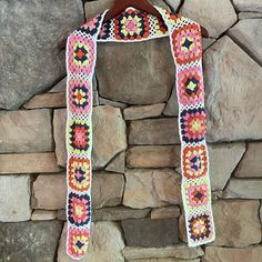 a crocheted scarf hanging on a stone wall next to a wooden hanger