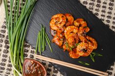 shrimp with sesame seeds and green onions on a black plate next to chopsticks