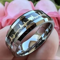 a close up of a person holding a wedding ring with heartbeats on it and flowers in the background