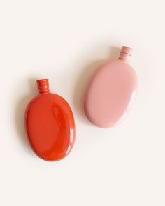 an orange and pink bottle sitting next to each other on a white surface with no one around it