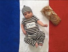 a baby dressed in jail clothes laying on a blanket next to a loaf of bread