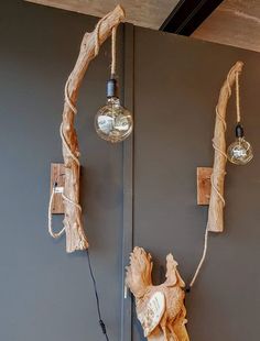 two light fixtures hanging from the side of a gray wall next to a wooden branch