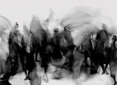 blurry photograph of people walking with umbrellas in the rain, black and white