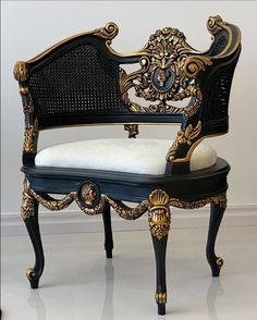 an ornate black and gold chair with white cushion on the armrests, sitting in front of a wall