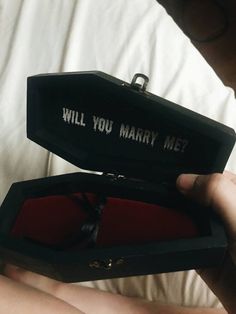 a person holding an open black box with the words will you marry me? written on it