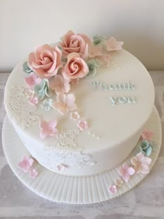 a white cake with pink and blue flowers on it's side that says thank you