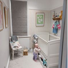 a baby standing in the corner of a room next to a crib with stuffed animals on it