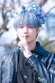 a young man with blue hair wearing a flower crown and blowing soap bubbles on his face