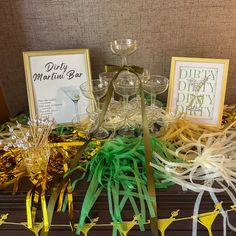 a table topped with lots of wine glasses and streamers next to framed signs that read dirty martini bar