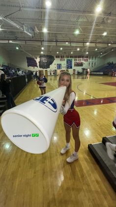 a cheerleader holding a large white cone in a gym with other cheerleaders