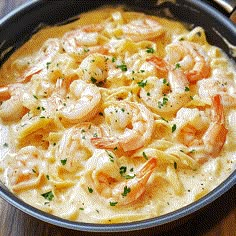 a bowl filled with pasta and shrimp on top of a wooden table