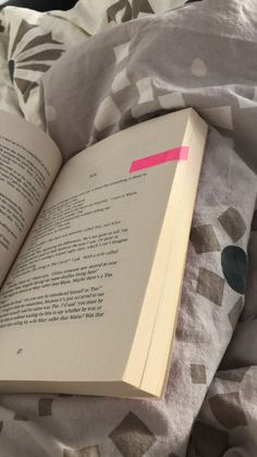 an open book sitting on top of a bed next to a white and pink blanket