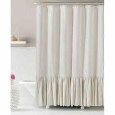 a white shower curtain with ruffles on the bottom, and a tub in the background