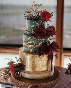 a three tiered wedding cake with red flowers on the top and gold trimmings