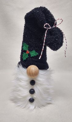 a black santa hat with holly and candy canes on it's head, hanging from a wooden stick