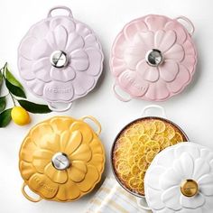 four flower shaped dishes sitting on top of a white table next to lemons and leaves