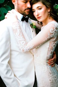 a bride and groom pose for a wedding photo in front of greenery at night