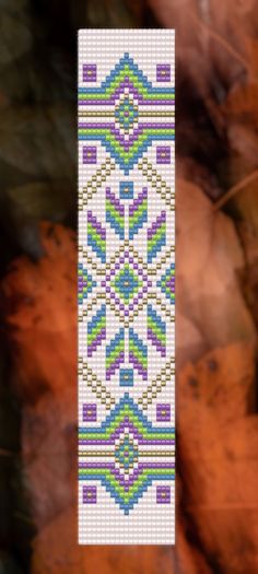 a cross - stitch bookmark hanging from a tree with leaves in the back ground