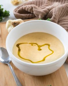 a white bowl filled with soup sitting on top of a wooden cutting board next to garlic