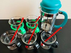 four cups with red and green straws next to a blender on a table