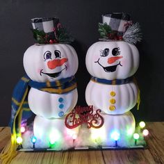 two snowmen with hats and scarfs on top of a wooden table covered in christmas lights