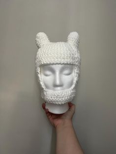 a person holding up a white knitted hat with ears