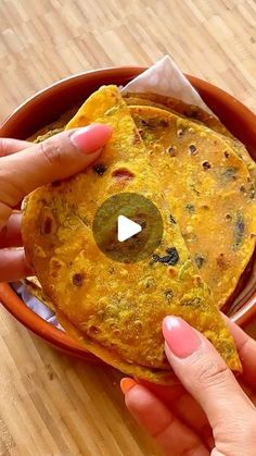 a person holding up a tortilla in a bowl on top of a wooden table