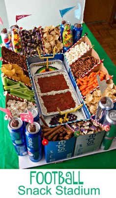 a football snack stadium is displayed with snacks and dips on the table, along with beer cans