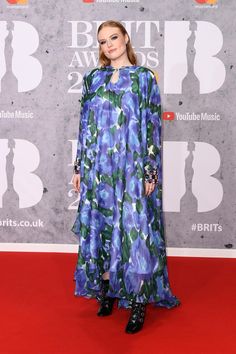 a woman standing on top of a red carpet wearing a blue and green dress with long sleeves