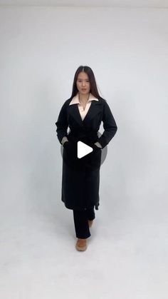 a woman standing in front of a white background wearing a black coat and brown shoes