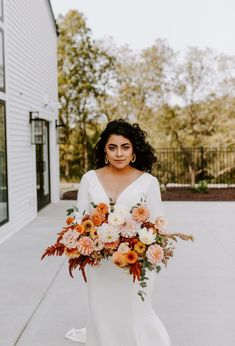 a woman in a white wedding dress holding a bouquet of orange and pink flowers on the sidewalk