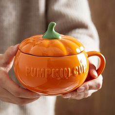 a person holding an orange pumpkin shaped container with the word pumpkin out on it's lid