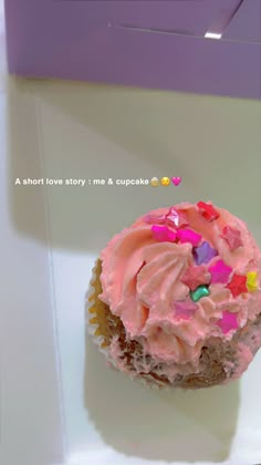 a cupcake with pink frosting and sprinkles on it's side