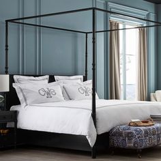 a four poster bed with white sheets and pillows in a blue room next to a window