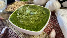 a white bowl filled with green pesto next to garlic and other ingredients on a table