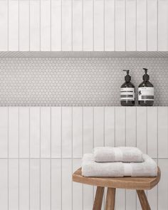 two white towels are sitting on a stool in front of a wall with hexagonal tiles