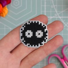 a hand holding a black and white beaded smiley face brooch with scissors in the background