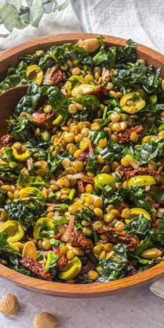 a wooden bowl filled with spinach salad and nuts on top of a white table