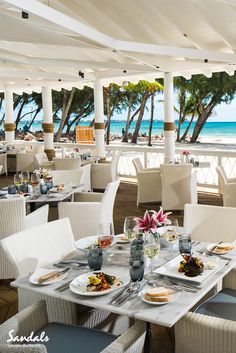 an outdoor dining area with white chairs and tables overlooking the ocean on a sunny day