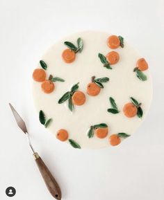 a cake decorated with oranges and leaves on top of a white plate next to a knife