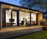 a small house with glass walls and wooden steps leading up to the outside patio area