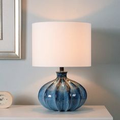 a blue vase sitting on top of a white table next to a clock and lamp